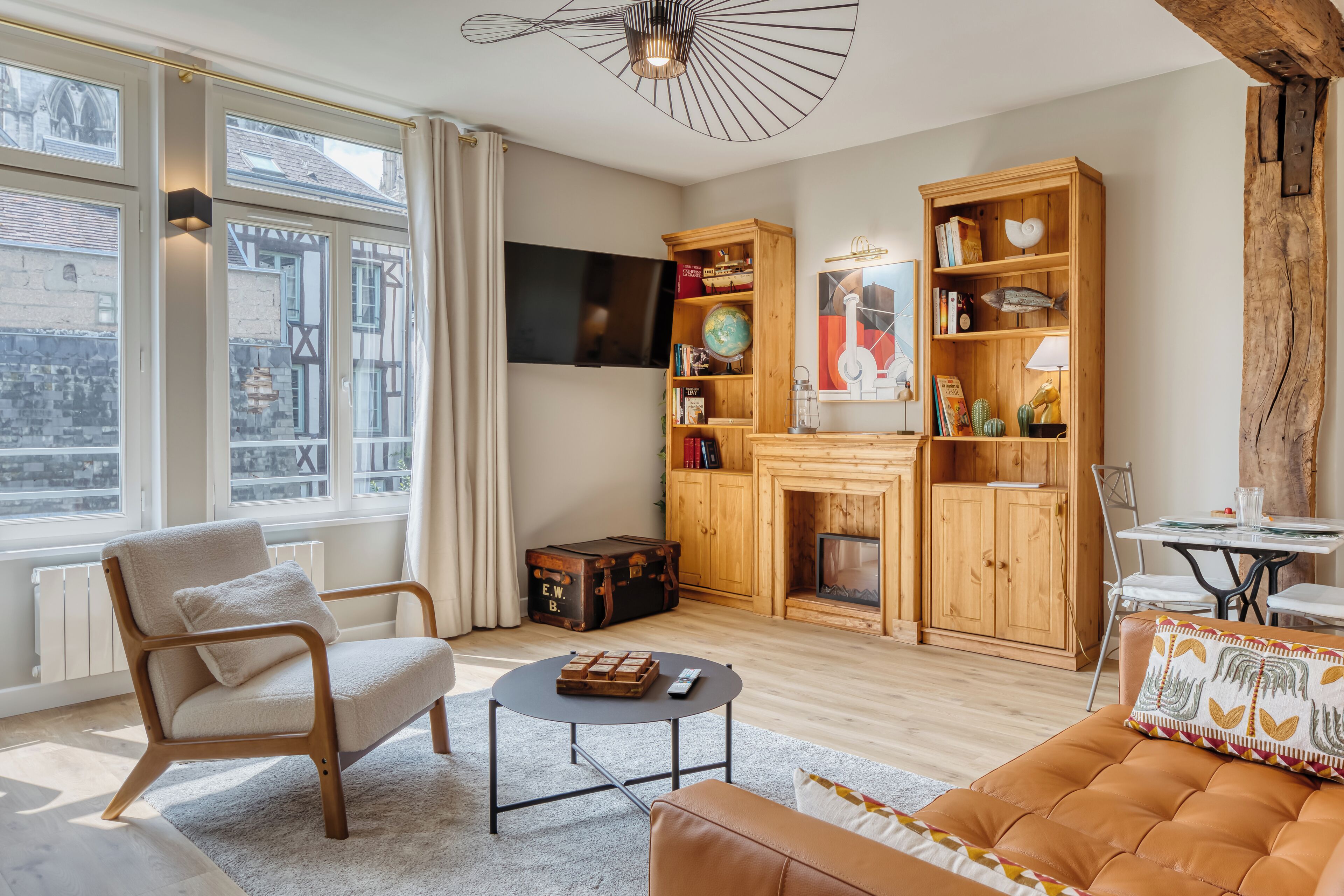 Ein Wohnzimmer mit Kamin, Fernseher, Bücherregal und einem Fenster mit Vorhängen.