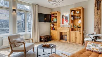Ein Wohnzimmer mit Kamin, Fernseher, Bücherregal und einem Fenster mit Vorhängen.