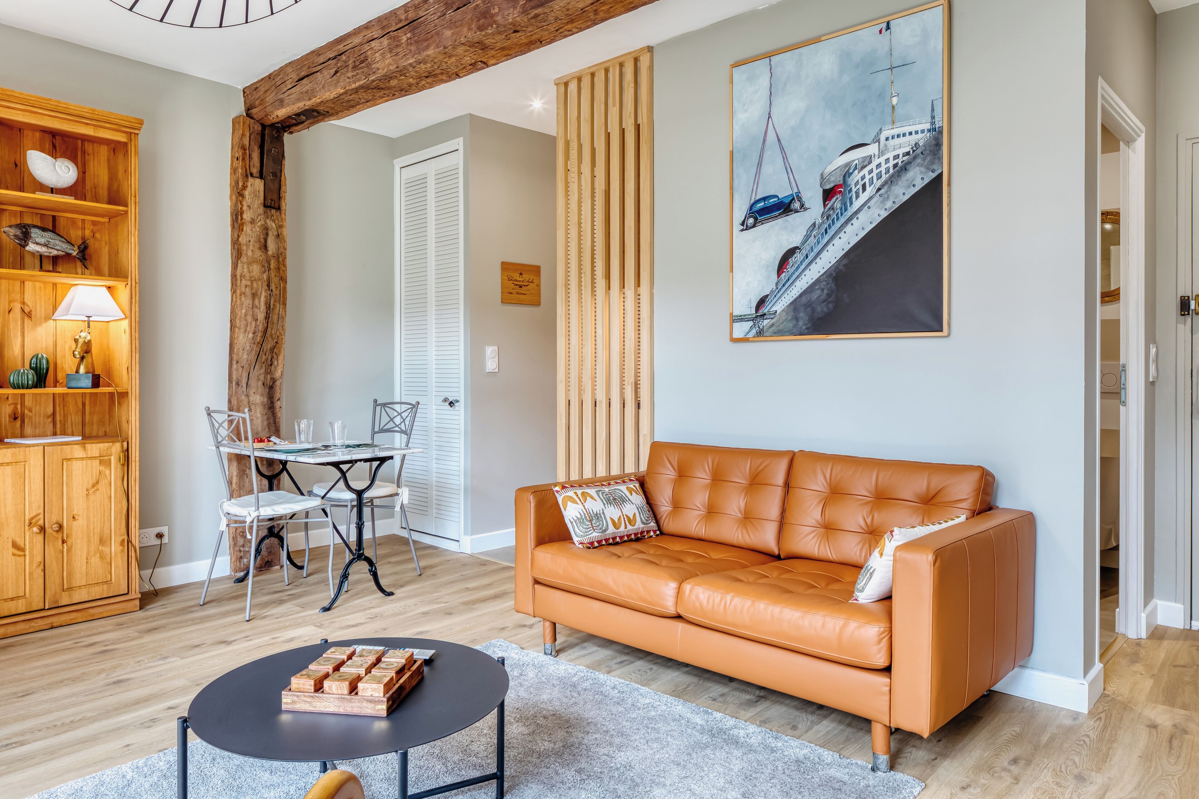 Un salon avec un canapé en cuir, une table à manger avec des chaises, un meuble en bois et un tableau accroché au mur.