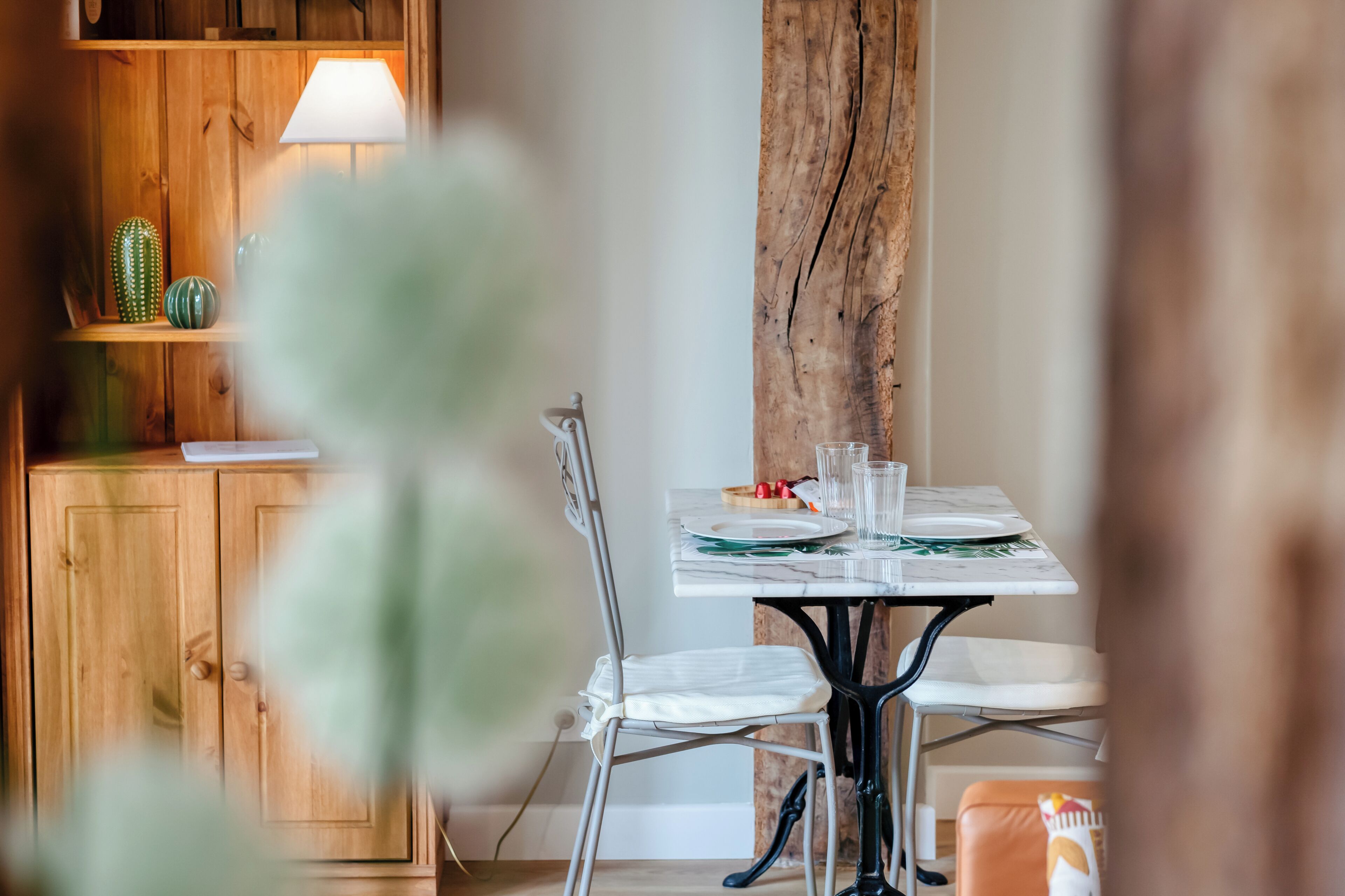 A dining area with a wooden cabinet, a lamp, a cactus, and a table set for two.