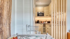 A modern kitchen with wooden cabinets, a built-in oven, and a dining area with a marble table and chairs. - La Venelle Saint-Nicolas (Rouen)