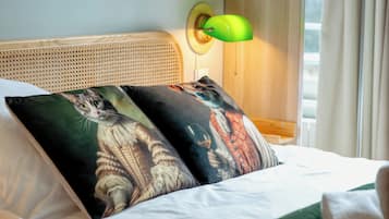 Una cama con dos almohadas decoradas con ilustraciones de gatos, una lámpara de pared verde y un cabecero de madera.