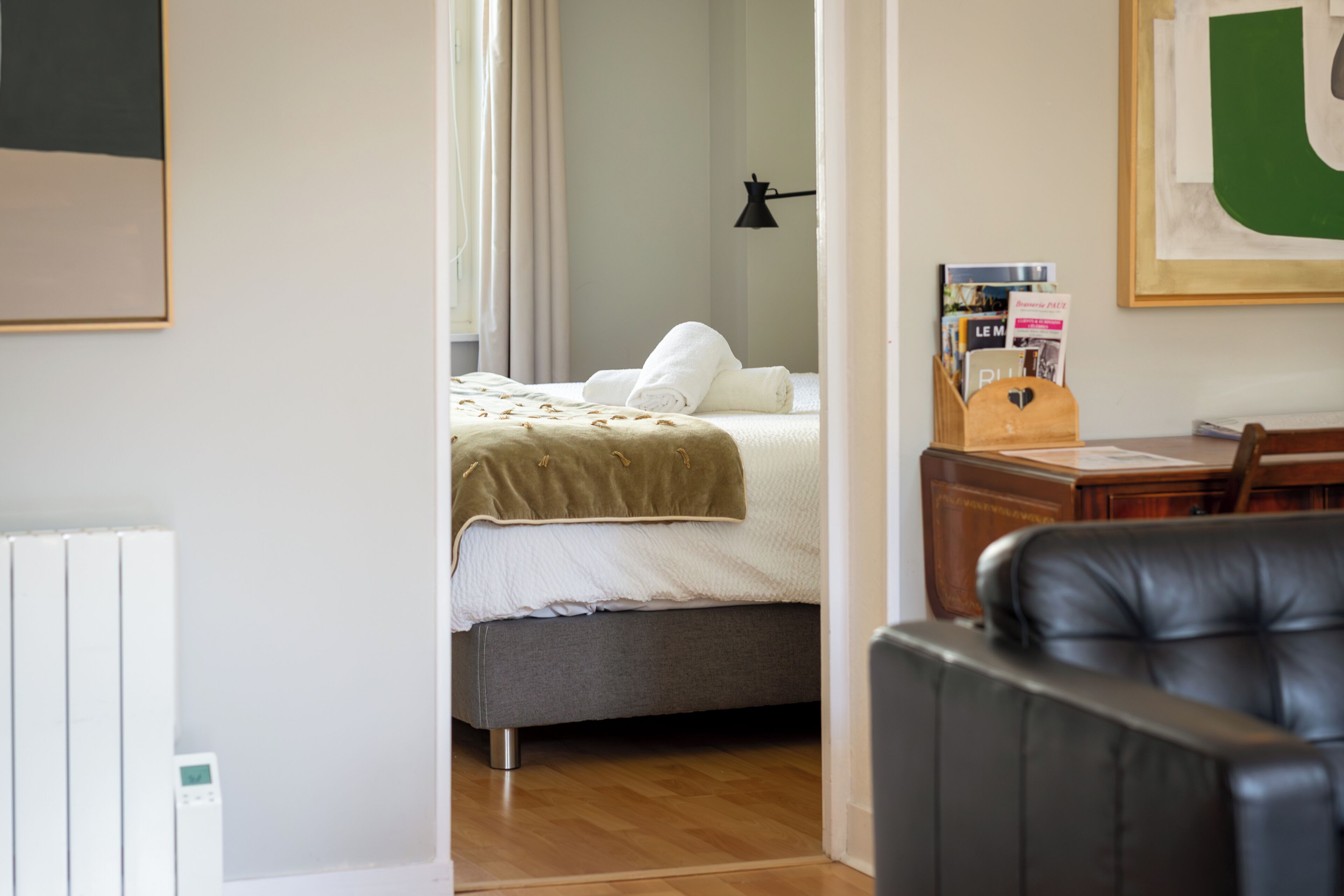 A bedroom with a bed, a desk, a chair, a radiator, and a framed picture on the wall.