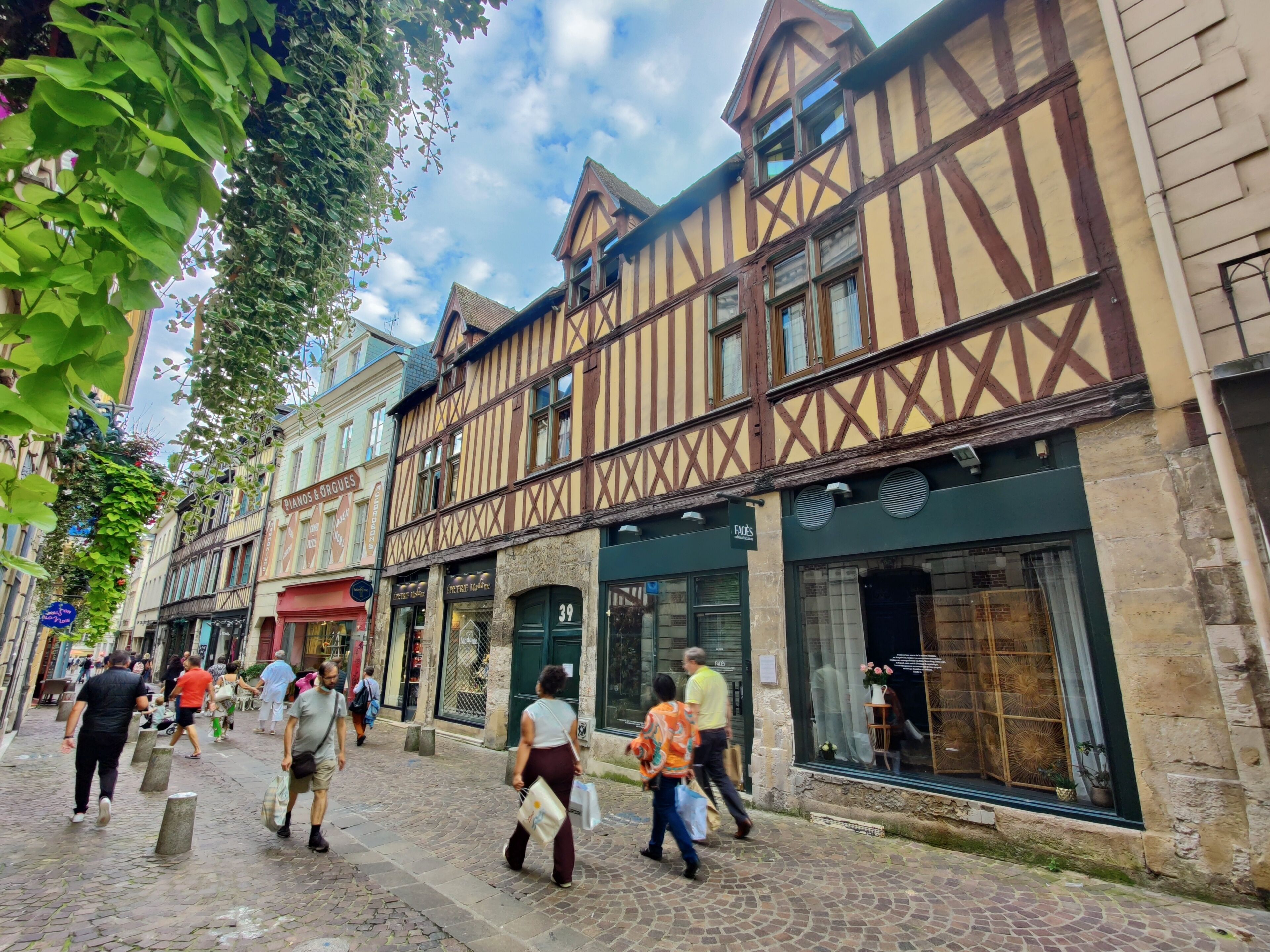 A cobblestone street lined with traditional half-timbered buildings, some with visible storefronts and signage.