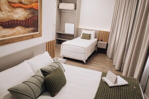 A hotel room with a bed, a bedside table, a nightstand, a wardrobe, and a painting on the wall. - HOTEL DAIELI (Otacílio Costa)