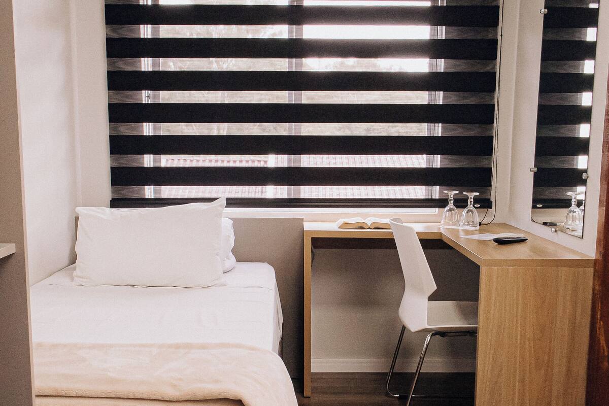 Habitación pequeña con cama, escritorio, silla y espejo.