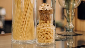 Drie glazen potten met pasta op een reflecterend oppervlak.