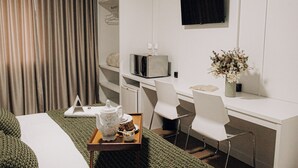 Een hotelkamer met een bed, een bureau met een computer, een televisie en een kleine tafel met een dienblad eten.