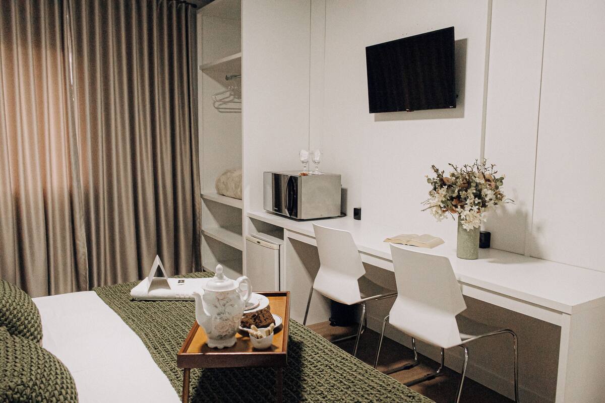 Habitación de hotel con una cama, un escritorio con computadora, un televisor y una mesita con una bandeja de comida.