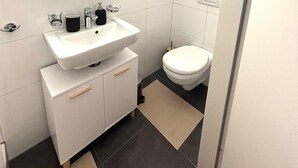 Un baño moderno con lavamanos, espejo y inodoro blancos.