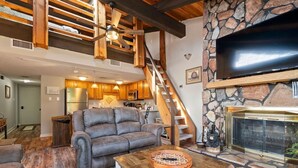 Un salón amplio con un sofá de cuero, una mesa de centro de madera, una chimenea de piedra y un televisor de pantalla plana grande montado en una pared de piedra.