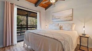 Un dormitorio con una cama grande, un ventilador de techo, una ventana con cortinas y un cuadro en la pared.