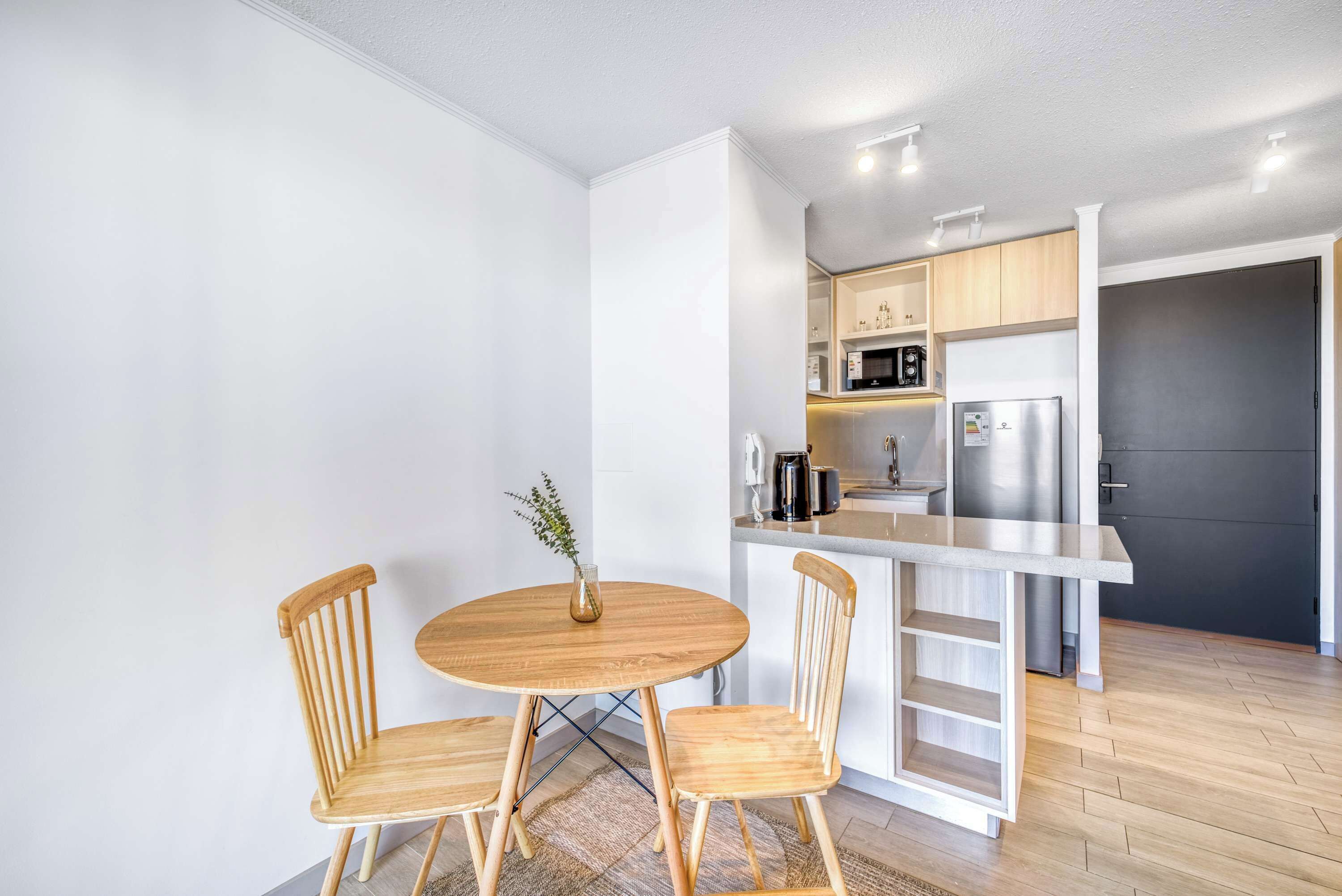 A modern kitchen with white cabinets, a stainless steel refrigerator, and a wooden dining table with chairs.