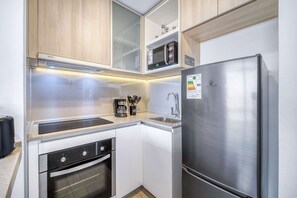 A compact kitchen with a built-in microwave, a stainless steel refrigerator, a dishwasher, and a coffee maker. - Duna Suite 1D con Vistas Hermosas (Concón)