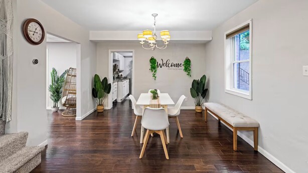 A dining area with a white table, chairs, and a bench. There is a clock on the wall and a 'Welcome' sign with greenery. - Suburban Buckhead Oasis - steps to beautiful park, playground, 5 min to midtown! (Atlanta)