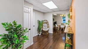 A hallway with a wooden floor, a white door, a wicker chair, and a dining area with a table and chairs. - Suburban Buckhead Oasis - steps to beautiful park, playground, 5 min to midtown! (Atlanta)
