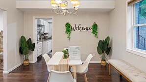 A dining area with a white table, chairs, a chandelier, and a welcome sign with greenery. - Suburban Buckhead Oasis - steps to beautiful park, playground, 5 min to midtown! (Atlanta)