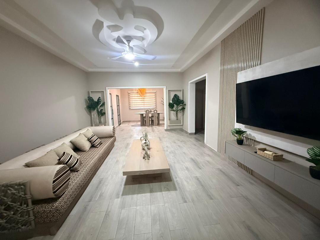 Una sala de estar moderna con un sofá, una mesa de centro, un televisor y un comedor al fondo.