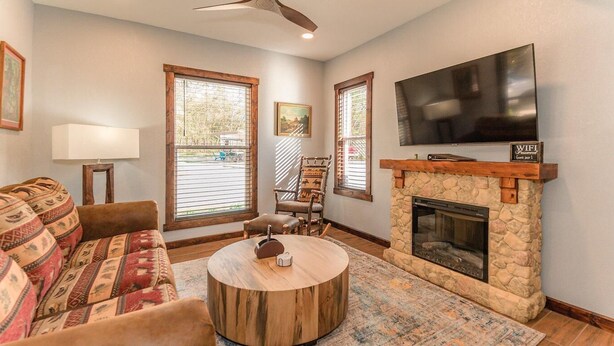 A living room with a fireplace, a television, a sofa, and a round coffee table. - Deluxe King One-Bedroom Cottage (Mobility Accessible) (Bronson)
