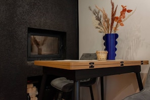 A room with a dark textured wall, a small framed picture, a wooden table with a blue vase, and a chair. - Cozy Studio at Pernavas 58 | Modern & Ground Floor (Rīga)
