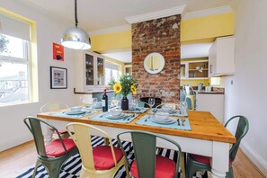 A dining area with a brick wall, wooden table, and chairs with red cushions. - Stylish Retro Retreat in Manchester, 4 Bed Home! (Greater Manchester)
