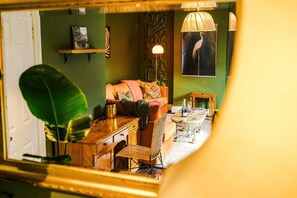 Ein Zimmer mit einer Couch, einem Sessel, einem Tisch, einer Lampe und einem Wandbild.