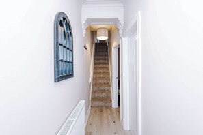 A narrow hallway with a wooden staircase, a radiator, and a window with a decorative frame. - Perfect Modern 4 Bed in Crewe, Great for Business (Cheshire East)