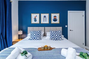 A hotel room with a bed, blue and white patterned bedding, a tray of pastries, and three framed artworks on the wall. - Perfect Modern 4 Bed in Crewe, Great for Business (Cheshire East)