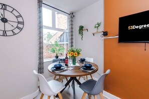 A dining area with a round table, chairs, a clock, and a TV on the wall. - Perfect Modern 4 Bed in Crewe, Great for Business (Cheshire East)