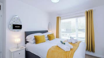 Habitació d'hotel amb llit, taula de nit, làmpada i finestra amb cortines.