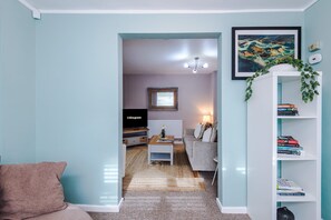 A living room with a sofa, a coffee table, a bookshelf, a framed picture, and a television. - Comfortable 4 Bed Home, Perfect for Business Stays (Elton)