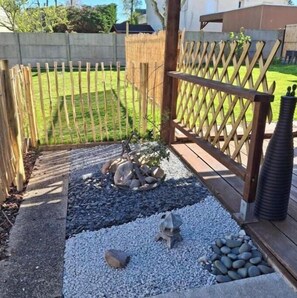 Un jardin avec une clôture en bois, des allées de gravier et un petit élément décoratif en roche.