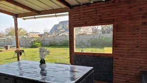 En udendørs terrasse med et overdækket siddeområde, udsigt til baghaven og en trævæg.