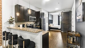 A modern kitchen with dark cabinets, a granite countertop, and a bar area with stools. - The Commodore Condo, Just 10 min to Broadway, Walk to Vandy/Centennial Park (Nashville)