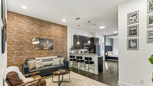 Un salon moderne avec un mur en briques, un canapé, une table basse et un coin cuisine équipé de tabourets de bar.