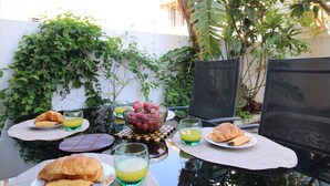 Ein Tisch mit Frühstücksangeboten, darunter Croissants, Trauben und Orangensaft, draußen mit Blick auf Grünflächen und ein Gebäude im Hintergrund.