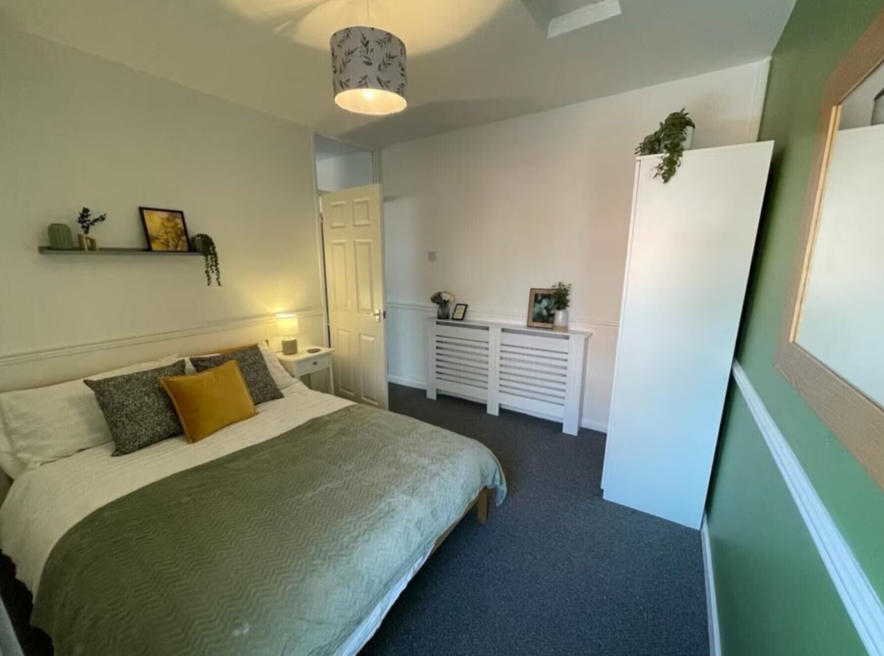 A bedroom with a bed, bedside table, lamp, and a dresser with a mirror.