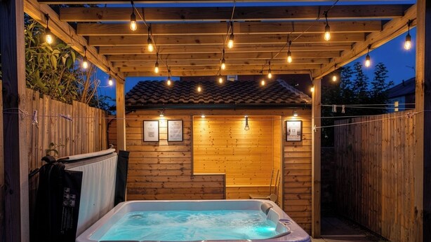Ein Whirlpool unter einer Holz-Pergola mit Lichterketten, umgeben von einem Holzzaun.
