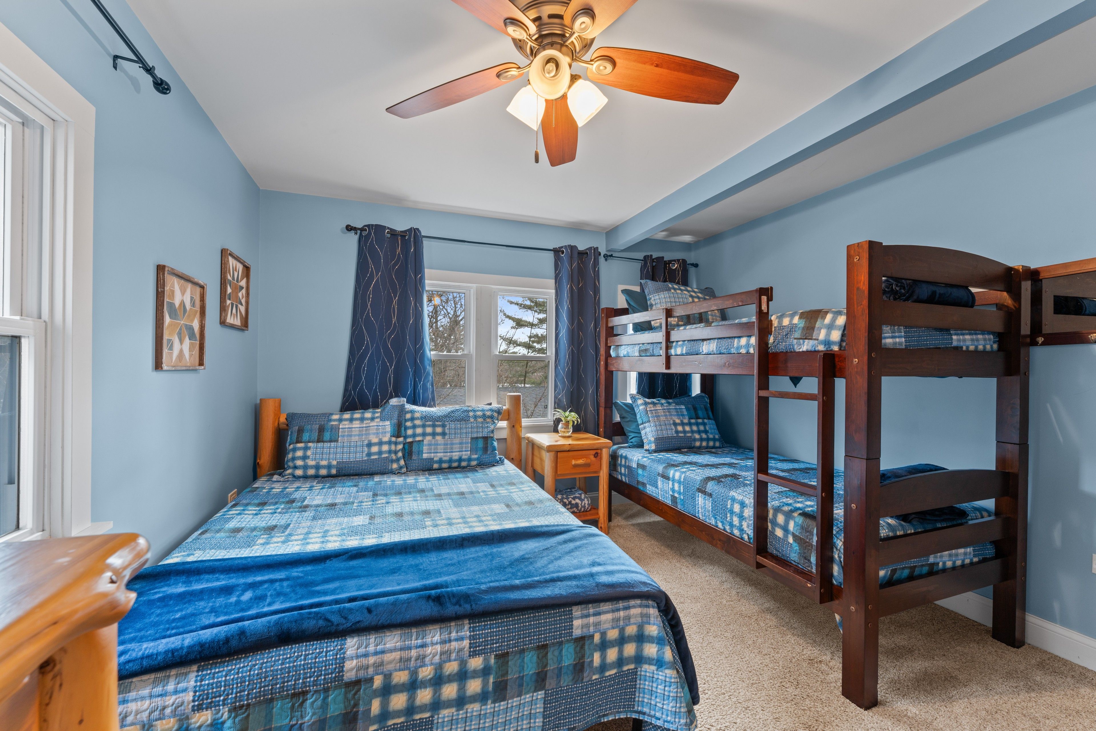Une chambre avec un lit superposé, un lit simple, un ventilateur de plafond et une fenêtre avec des rideaux.
