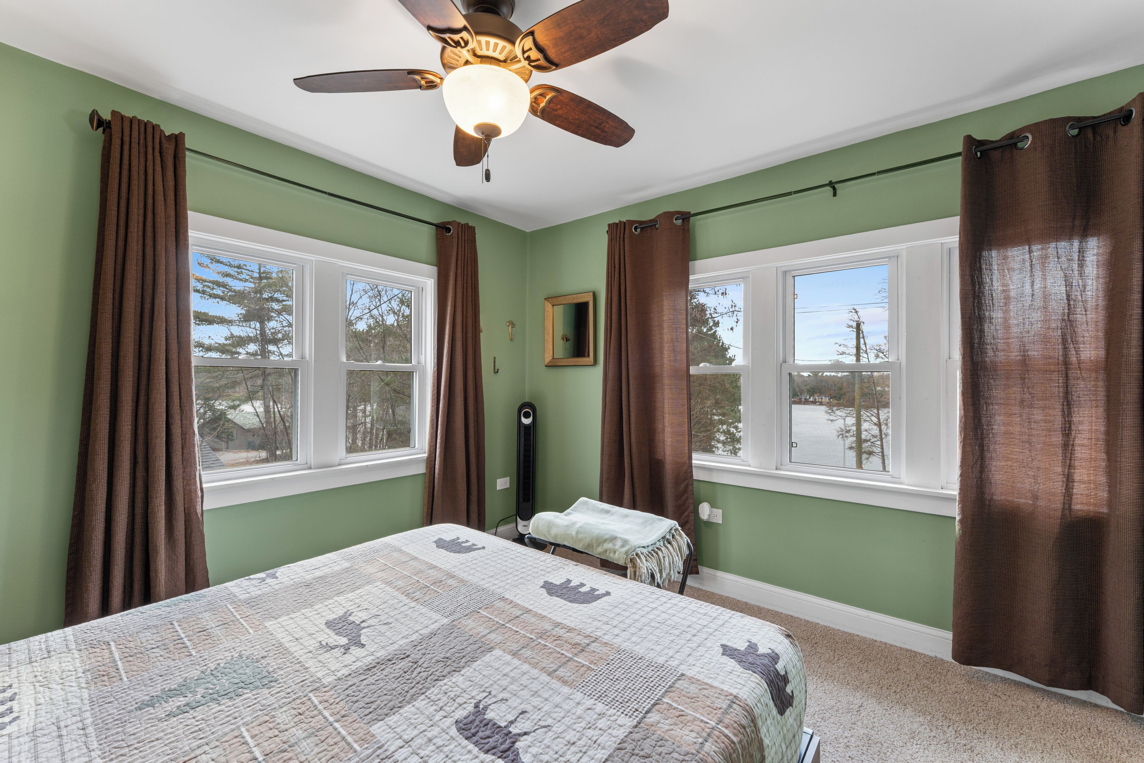 A bedroom with a bed, a ceiling fan, two windows, and a view of the outdoors.