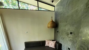 Un salon moderne avec un canapé d’angle, un luminaire suspendu et une grande fenêtre.