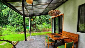 Un espace extérieur abrité, doté d’un évier, d’une table en bois et de chaises, le tout entouré de verdure.