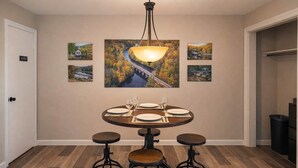 A dining area with a round table, four stools, and a hanging light fixture.