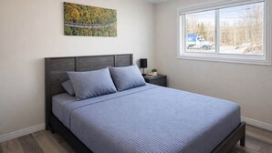 A bedroom with a bed, a nightstand, a window, and a painting on the wall.