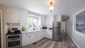 A modern kitchen with white cabinets, stainless steel appliances, a wooden floor, and a window with a view.