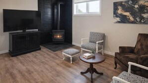 A living room with a TV, black cabinet, fireplace, patterned chairs, and a painting on the wall.