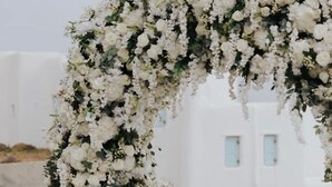 An outdoor wedding arch with white flowers, a white building in the background, and a clear sky. - Atlas in Mykonos With 8 Bedrooms and 8 Bathrooms (Mykonos)