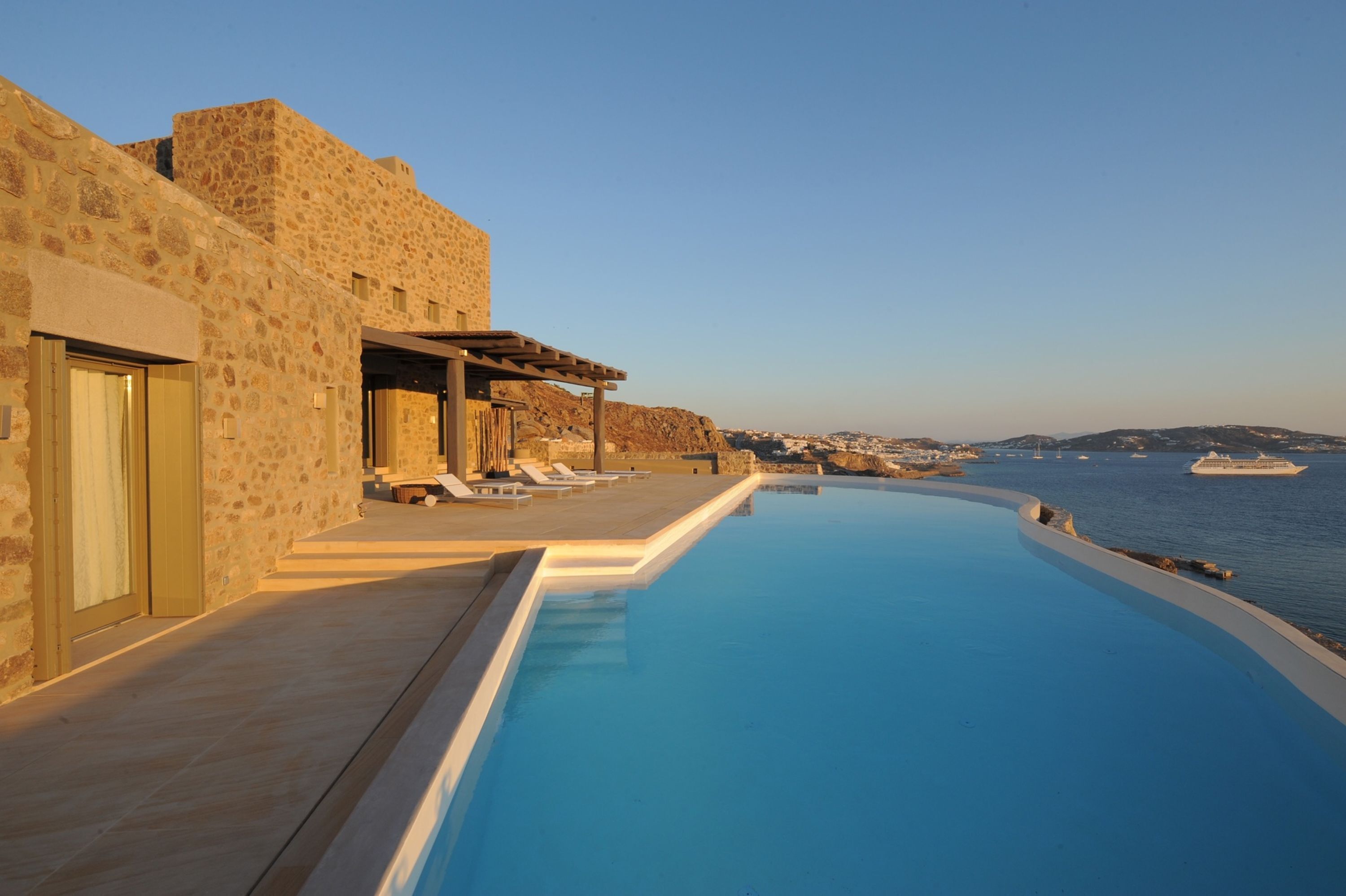 Un edificio de piedra con piscina y sillones de descanso con vistas al mar.