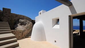 Un edificio moderno con un muro de piedra, fachada blanca y vista al mar.