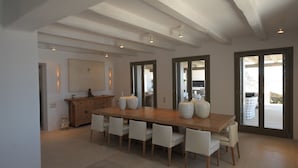 Un comedor amplio con una larga mesa de madera, sillas blancas y grandes jarrones.